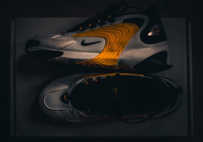 A pair of modern athletic shoes featuring a sleek design with curved lines and a blend of white, black, and vibrant orange hues. The shoes are displayed from a side and top view, highlighting their dynamic style and brand logo.