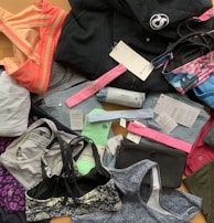 A collection of various athletic apparel and accessories laid out, including sports bras, tops, headbands, and tags. The items are in different colors and patterns, such as pastel pink, blue, and floral designs. A black jacket and several pieces still have brand tags attached.