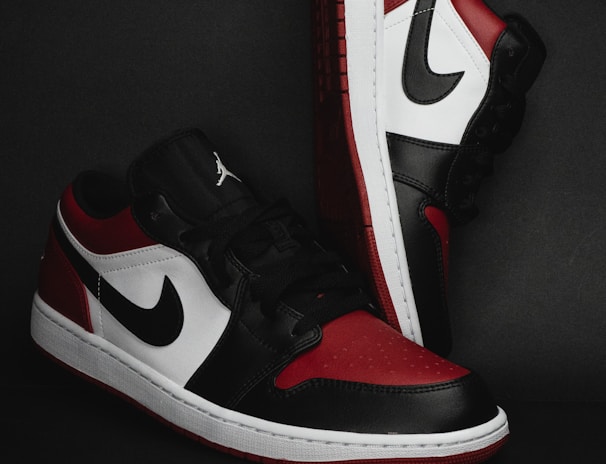 A pair of stylish athletic shoes in black, white, and red colors with distinctive branding. The shoes are positioned against a dark background, showcasing their sleek design and detailed craftsmanship.