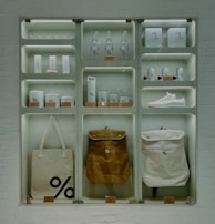 A well-organized display of branded merchandise with a minimalist aesthetic. The items include bottles, cups, a sneaker, bags, and other accessories, all featuring a distinctive percentage symbol on a white or neutral background. The display is set against a white brick wall, giving an industrial feel.