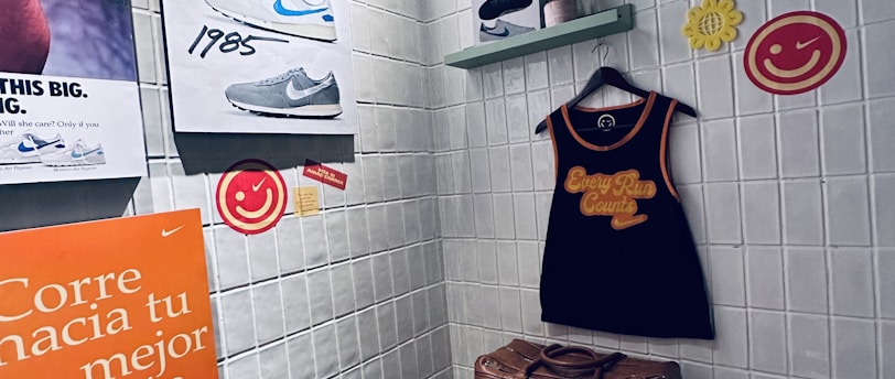 A small retro-themed display with a focus on athletic apparel and shoes. The walls feature a series of posters showcasing various Nike shoes from different years. A black gym tank top and a brown leather gym bag are prominently positioned on a wooden bench. There are decorative elements like potted plants on wall-mounted shelves and smiley face icons. The environment has a nostalgic and sporty atmosphere.