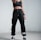 A person stands confidently indoors, wearing black athletic clothing including a crop top and sweatpants. They are also wearing sunglasses, sneakers, and have a watch on their wrist. The stance is assertive, with one hand pointing forward.