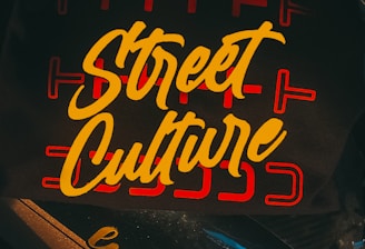 A dark background is overlaid with the bold, yellow cursive text 'Street Culture' featured prominently on a surface. The text is surrounded by red linear designs, adding an urban artistic touch. Below, the words 'lutte pro' are printed on part of a motorbike.