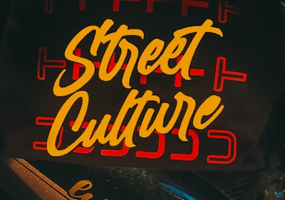 A dark background is overlaid with the bold, yellow cursive text 'Street Culture' featured prominently on a surface. The text is surrounded by red linear designs, adding an urban artistic touch. Below, the words 'lutte pro' are printed on part of a motorbike.